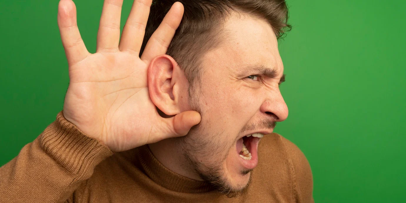 close-up-view-curious-young-blonde-handsome-man-keeping-hand-ear-looking-straight-doing-i-can-t-hear-you-gesture_141793-114840 Hombre con perdida auditiva o hipoacusia haciendo gesto de escuchar