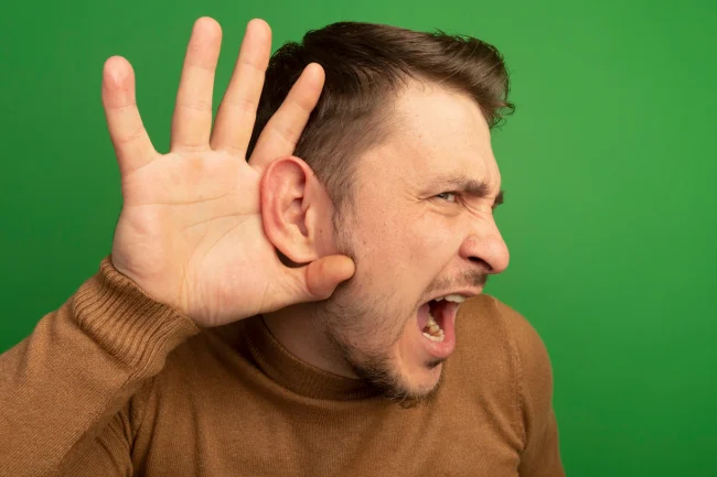 close-up-view-curious-young-blonde-handsome-man-keeping-hand-ear-looking-straight-doing-i-can-t-hear-you-gesture_141793-114840 Hombre con perdida auditiva o hipoacusia haciendo gesto de escuchar